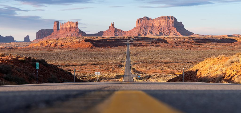 Monument Valley from afar with an empty stretch of road as far as the eye can see.