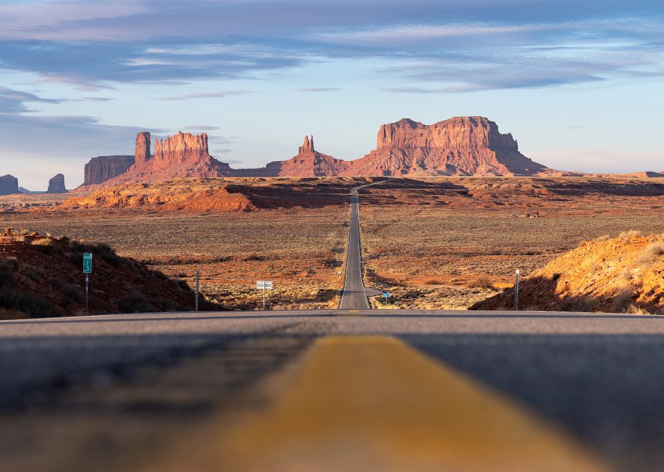 Monument Valley from afar with an empty stretch of road as far as the eye can see.
