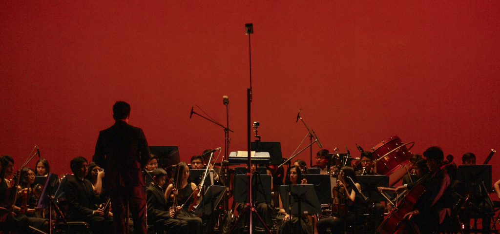 An orchestra performing in front of a deep red background.